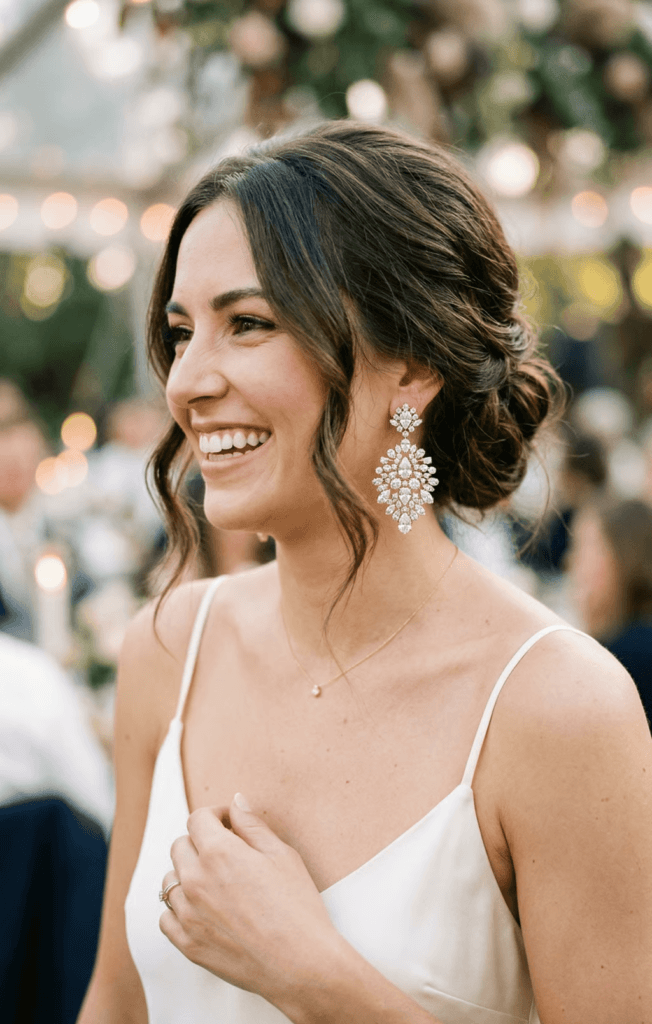 A close-up of a smiling bride wearing sparkling statement earrings to complement her elegant wedding reception outfit.